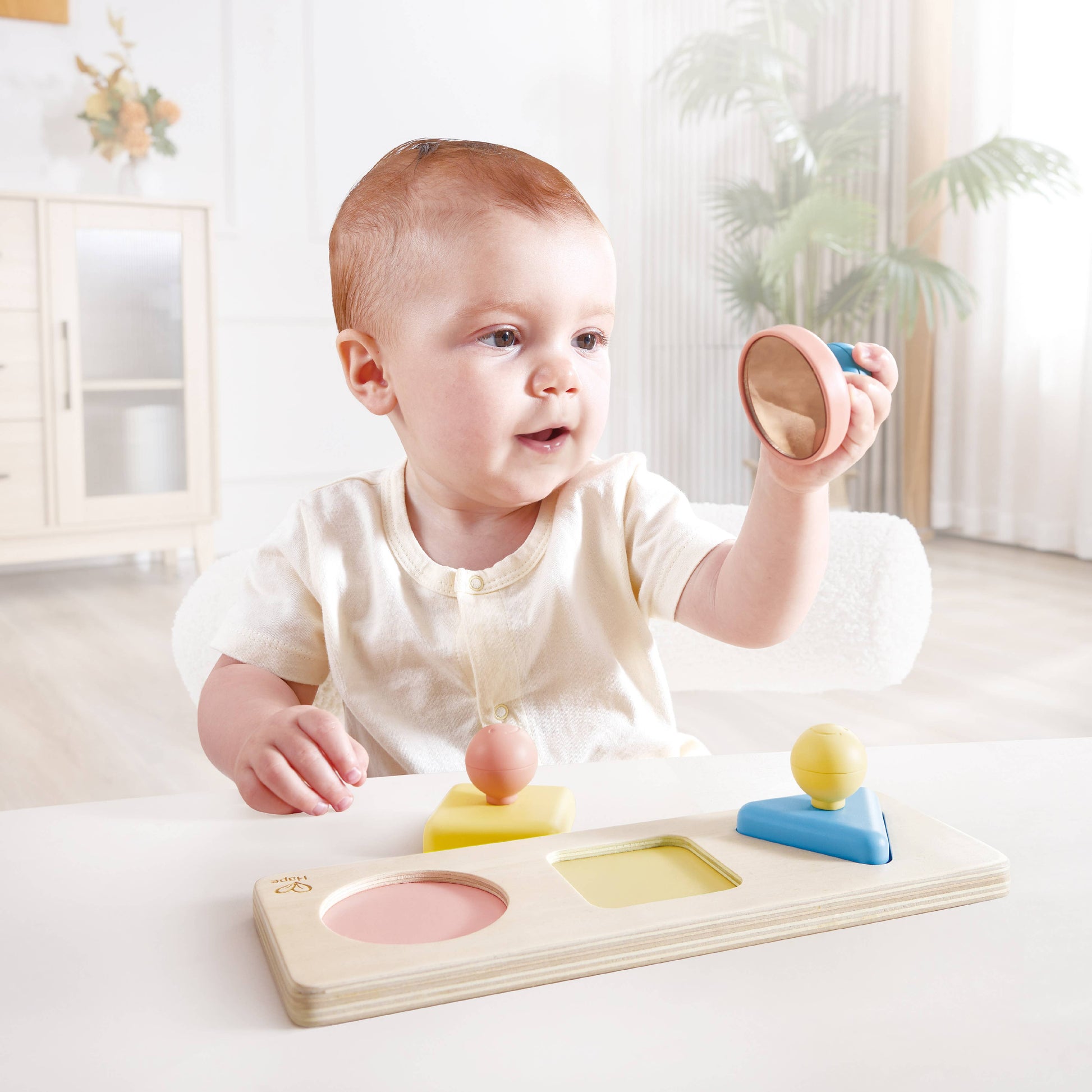 Baby playing with a wooden shape sorting toy in a bright room.