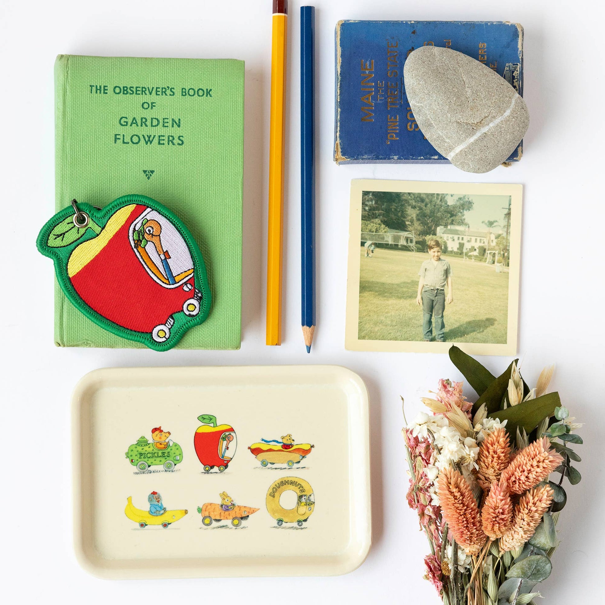 Collection of items including a green book, colorful patch, pencil, photo, and decorative tray on a white surface.
