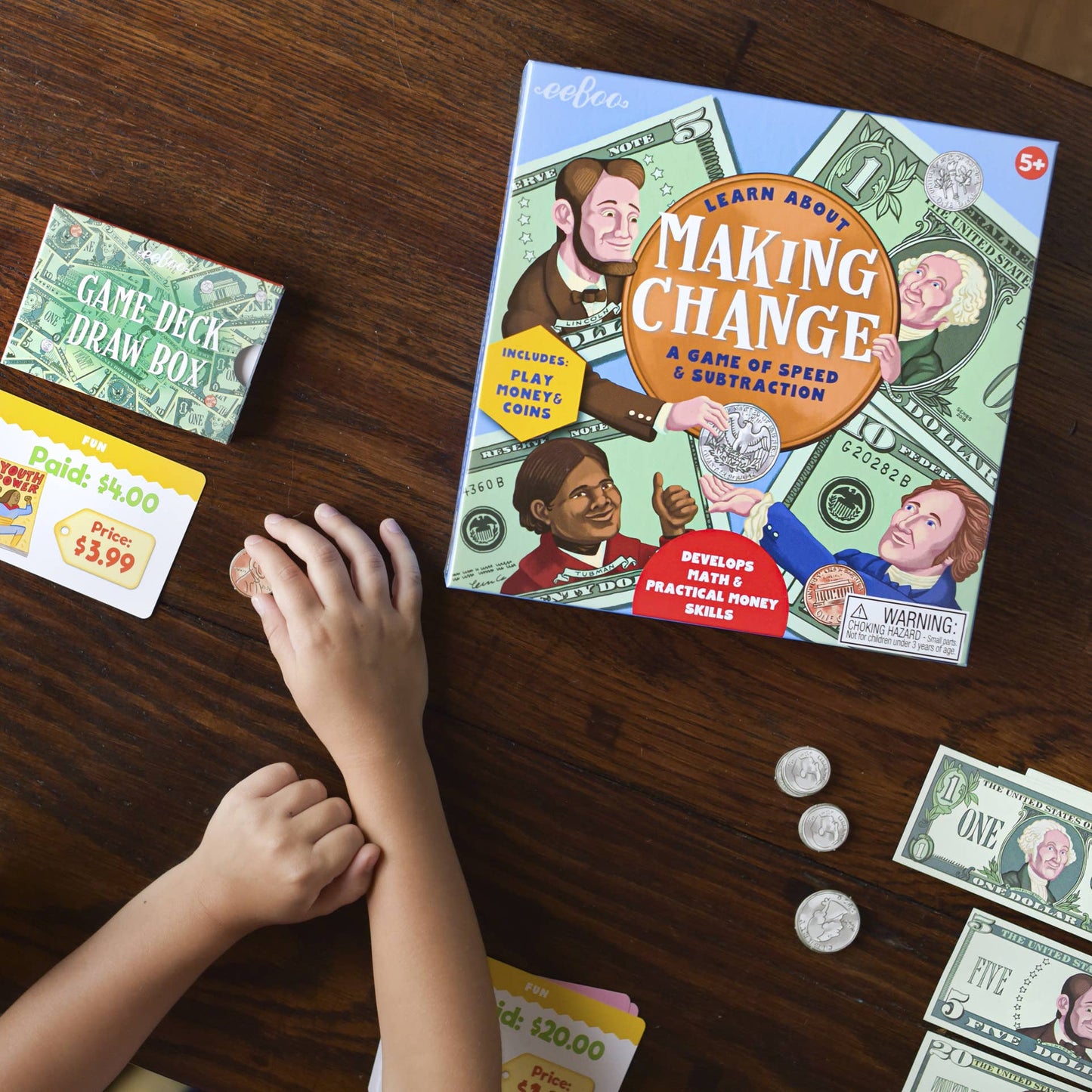 Children's educational game 'Making Change' on a wooden table with money and cards.