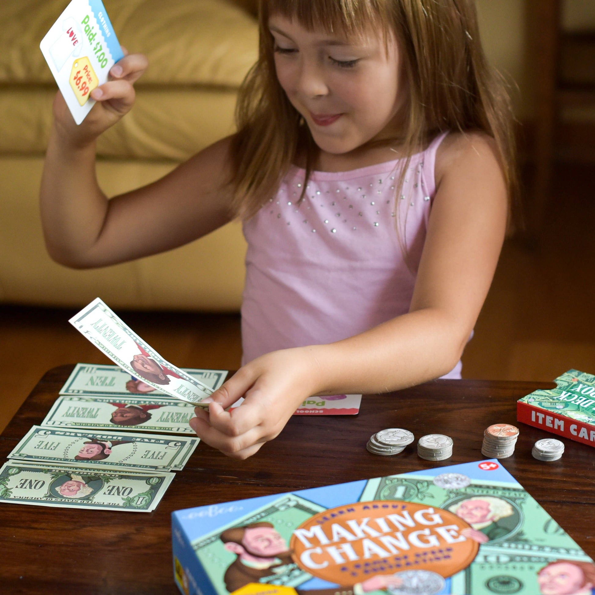 Young girl playing with money and a 'Making Change' game box on a table.