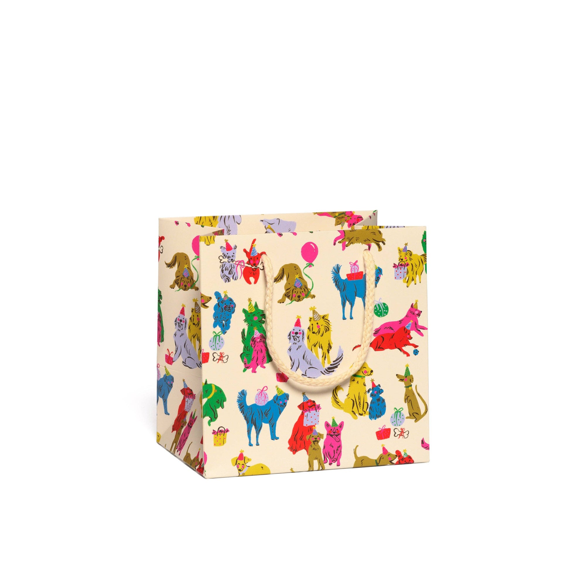 A small gift bag with a cream-colored base covered in a colorful cartoon dog pattern, featuring two light beige paper handles, shown on a plain white background.