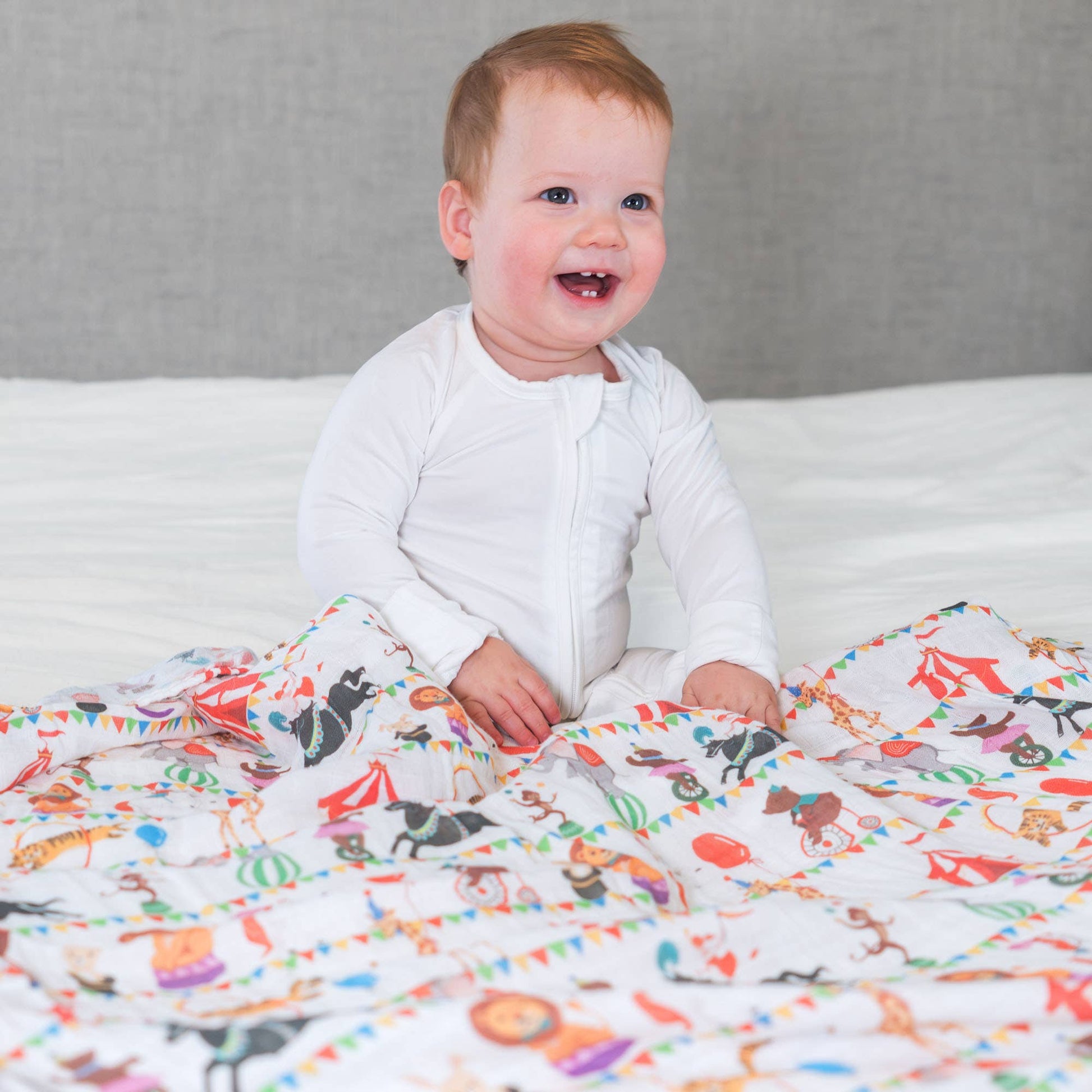 Baby sitting on a bed with a colorful animal-patterned blanket