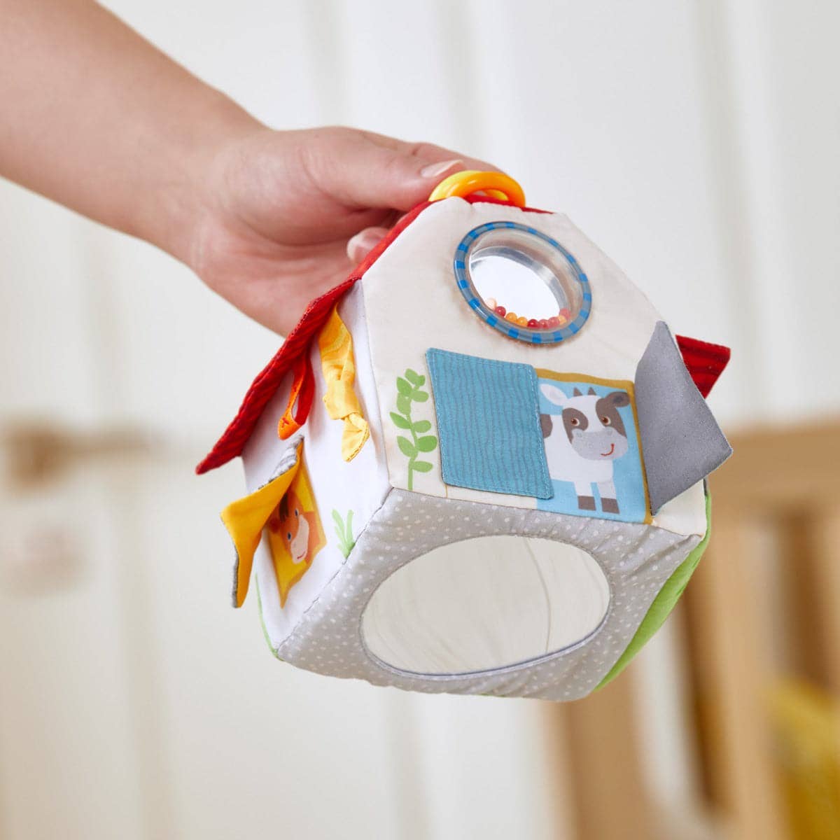 Colorful baby toy held by a hand against a neutral background