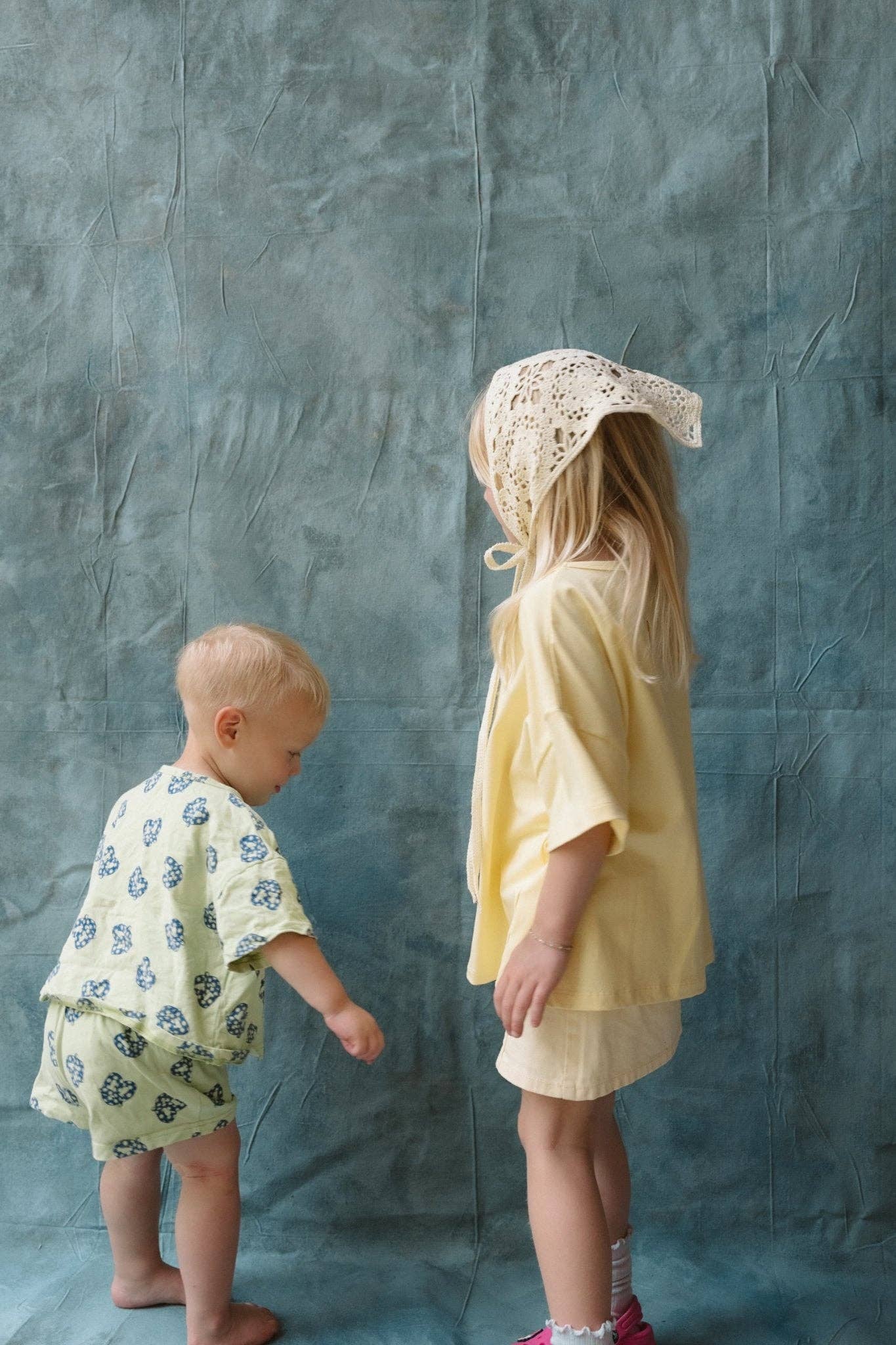 Two children in patterned outfits standing against a textured gray background
