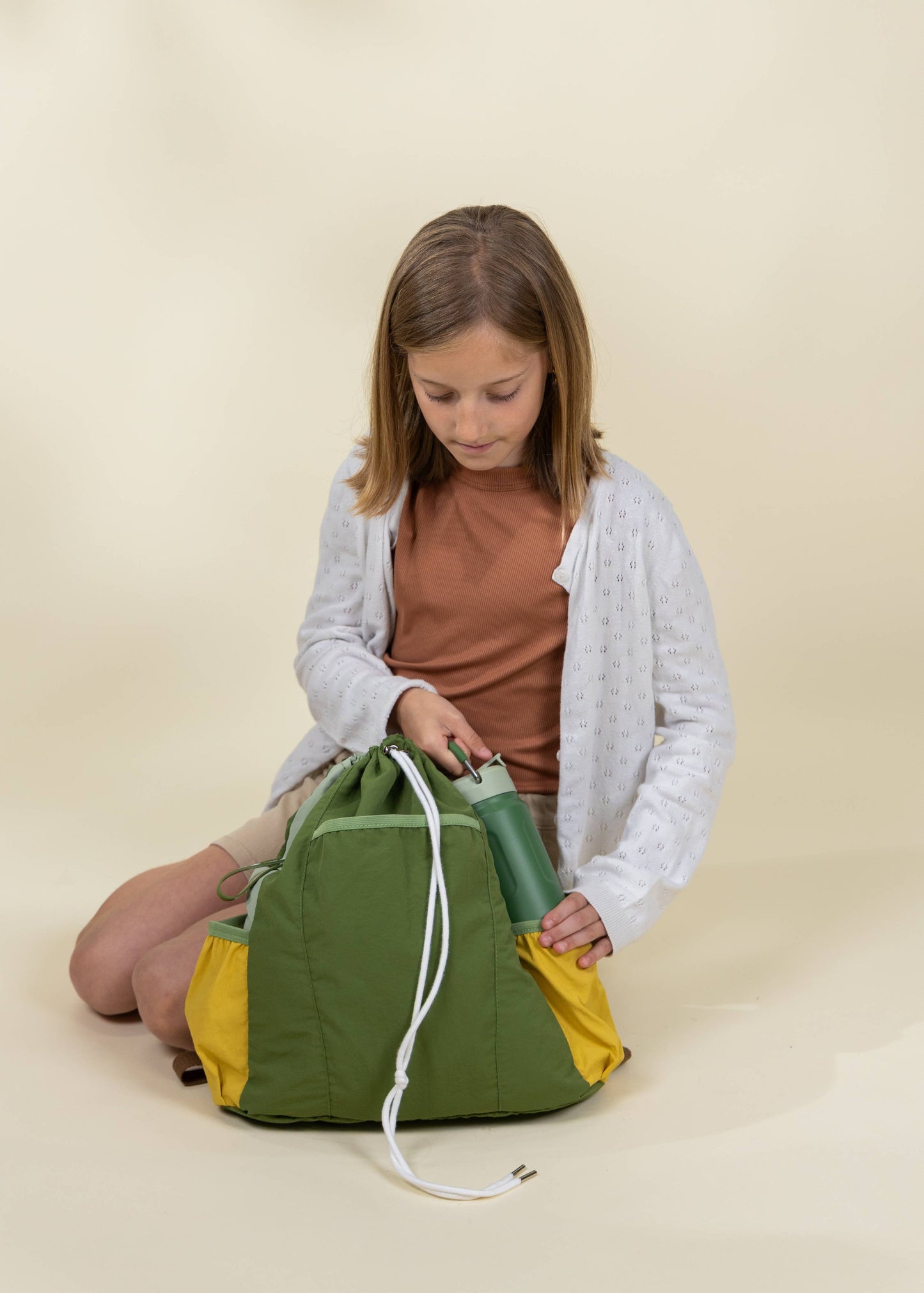 Girl opening a green and yellow bag on a beige background