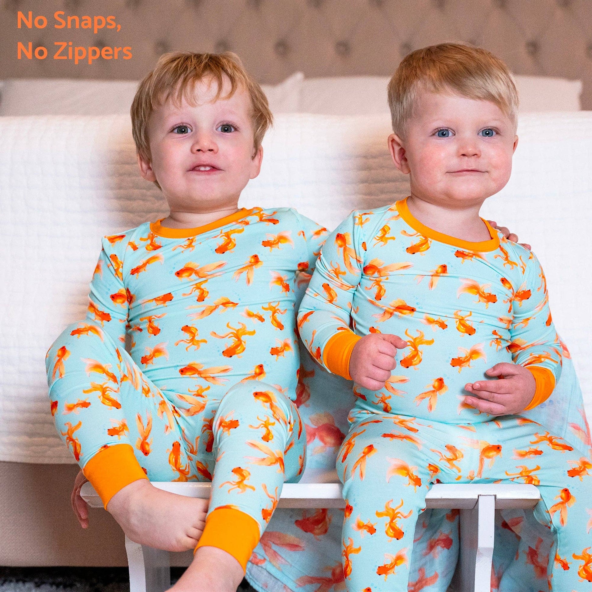 Two children wearing matching pajamas with a pattern of orange fish on a light blue background.