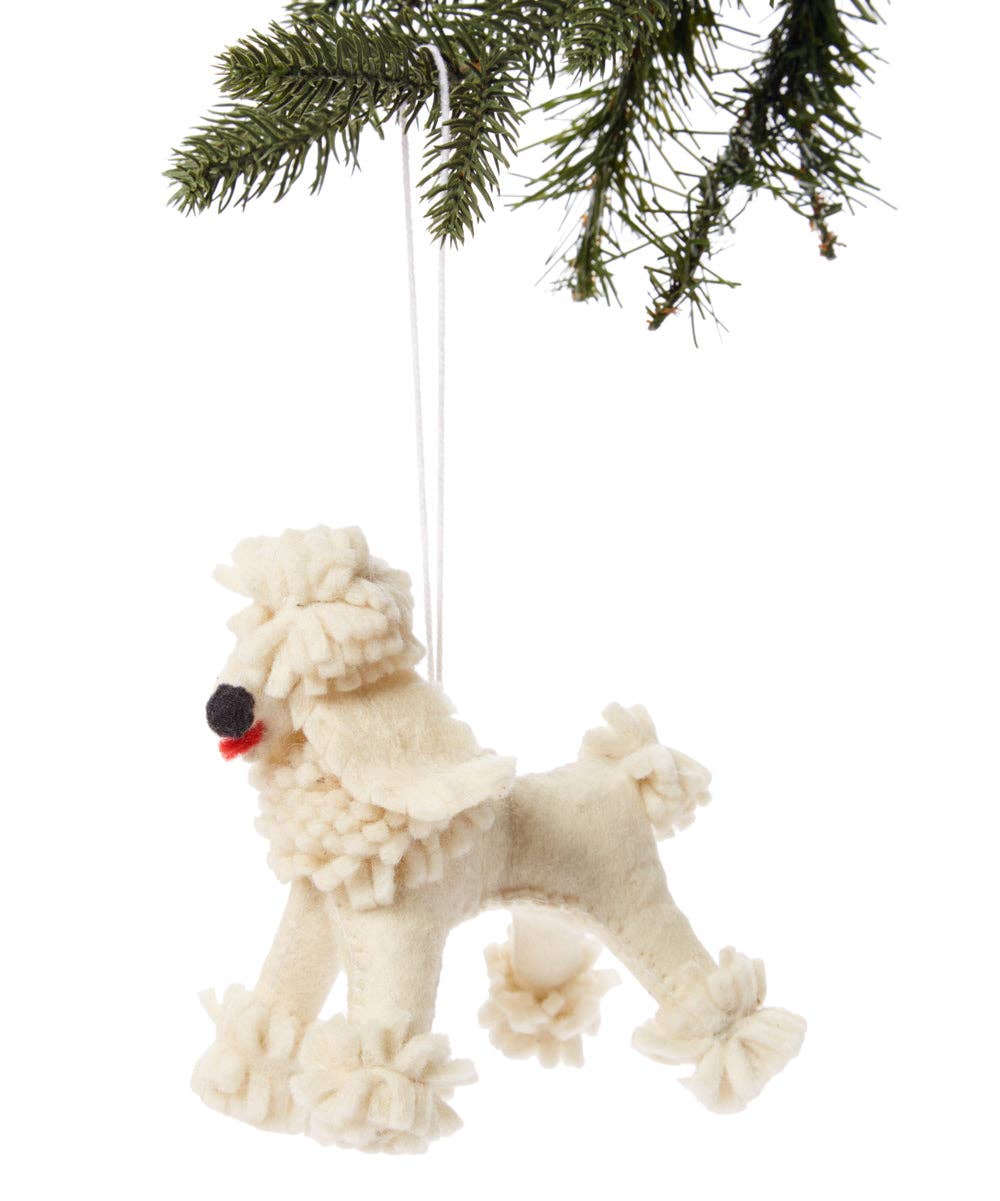 A cream-colored felt poodle Christmas ornament hanging from a green pine tree branch against a white background.