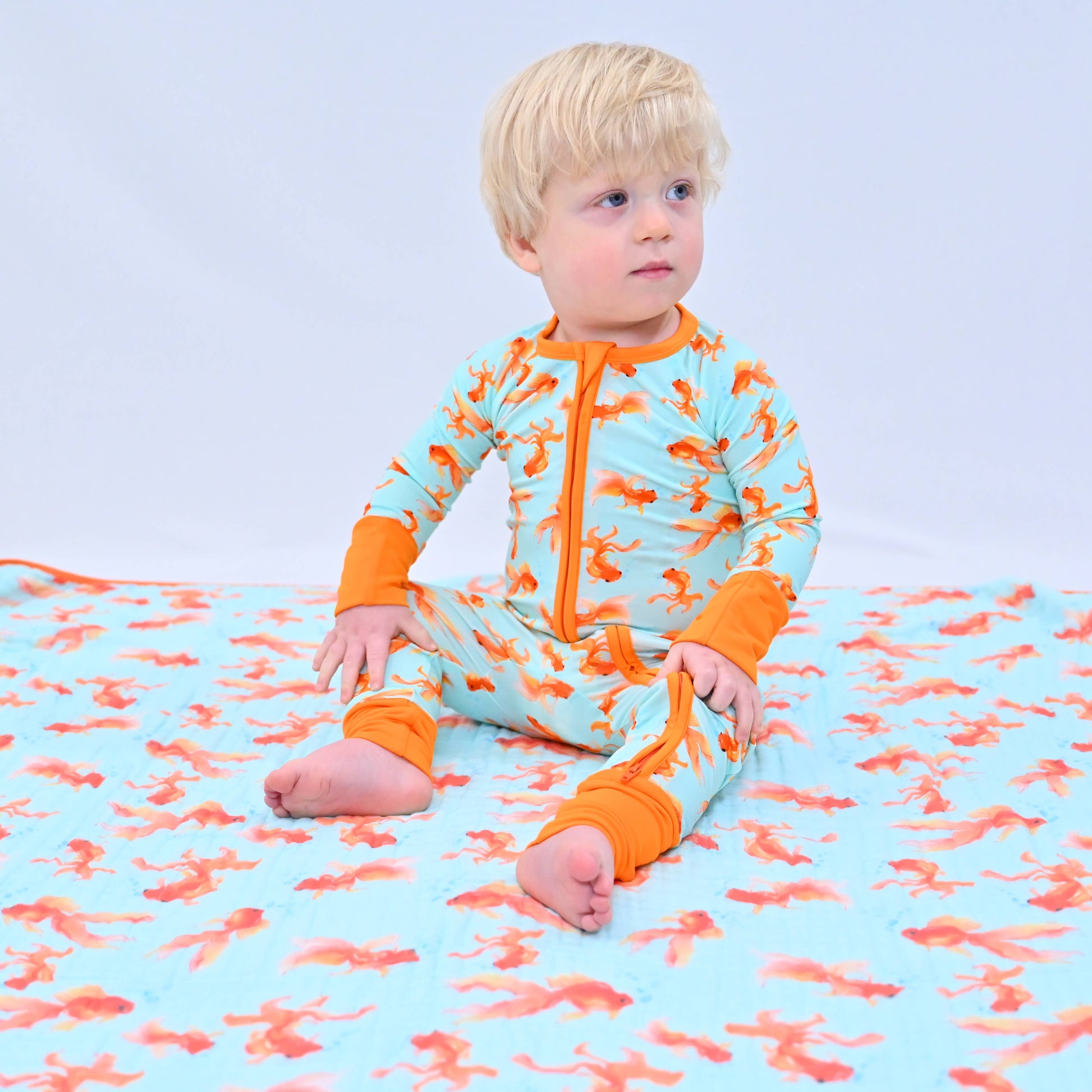 Child wearing a colorful pajama onesie sitting on a matching blanket with a blue background