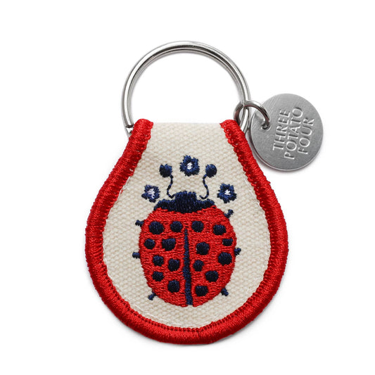 Keychain with a ladybug design and 'Three Potato Four' tag on a white background