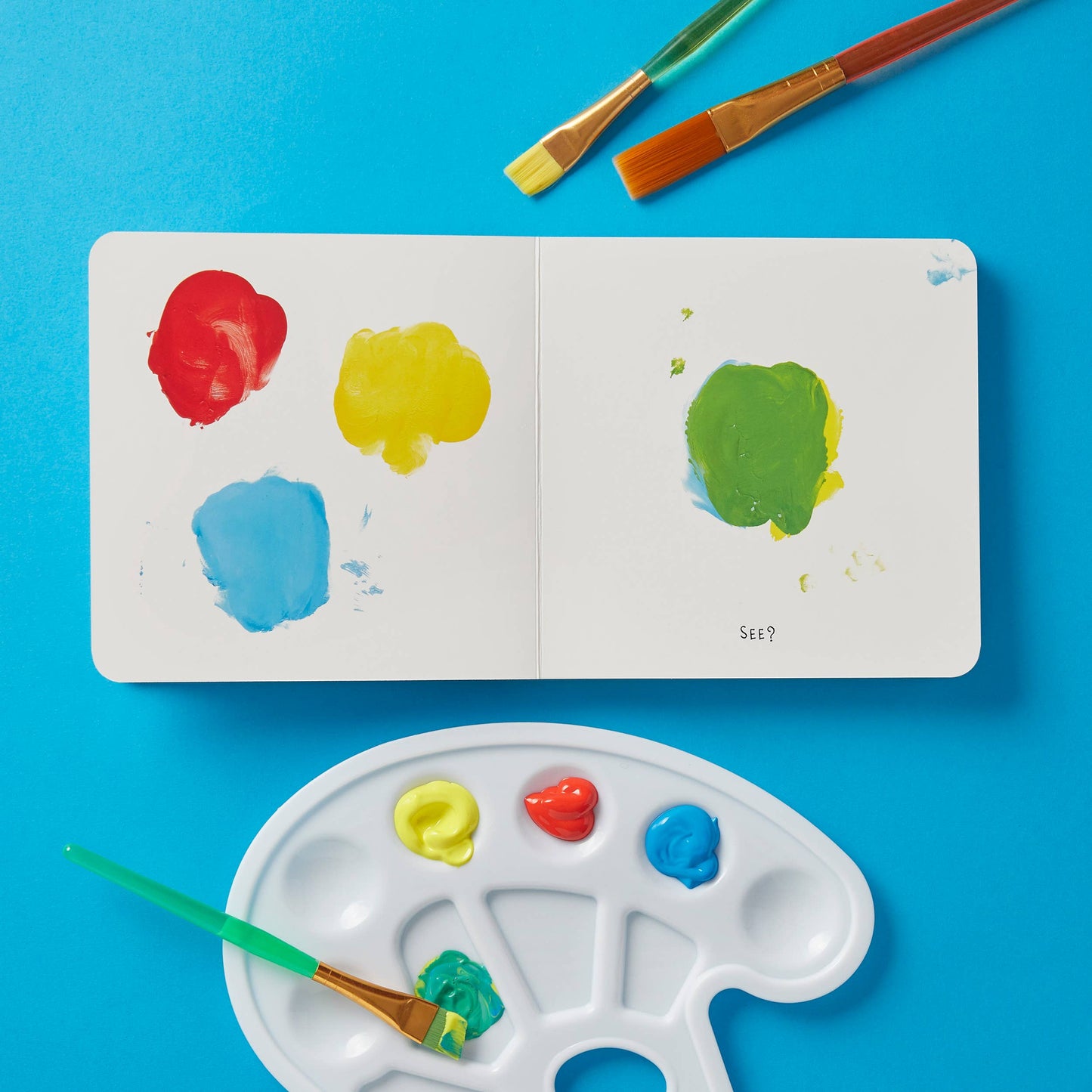 Color swatches on a small book with paintbrushes and a palette on a blue background