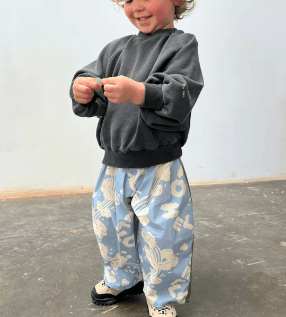 Child wearing a gray sweatshirt and blue patterned pants standing on a plain background