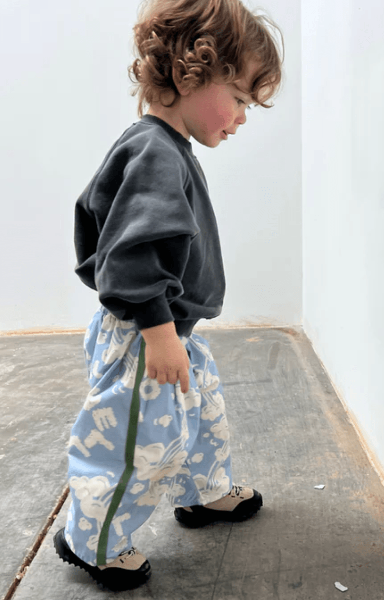 Child wearing a dark gray sweatshirt and light blue pants with white patterns on a plain background
