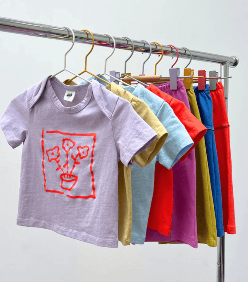 Children's colorful clothing on hangers with a purple shirt featuring a red design.
