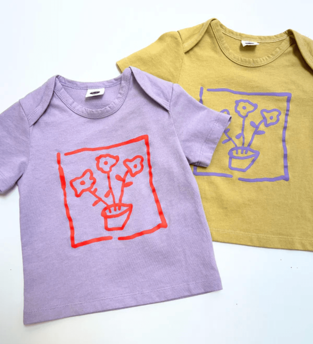 Two children's t-shirts, one purple and one yellow, with flower graphics on a white background.