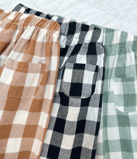 Three pairs of plaid pants, one brown and white, the other black, gray, and white,and a third in green and white  on a light background.