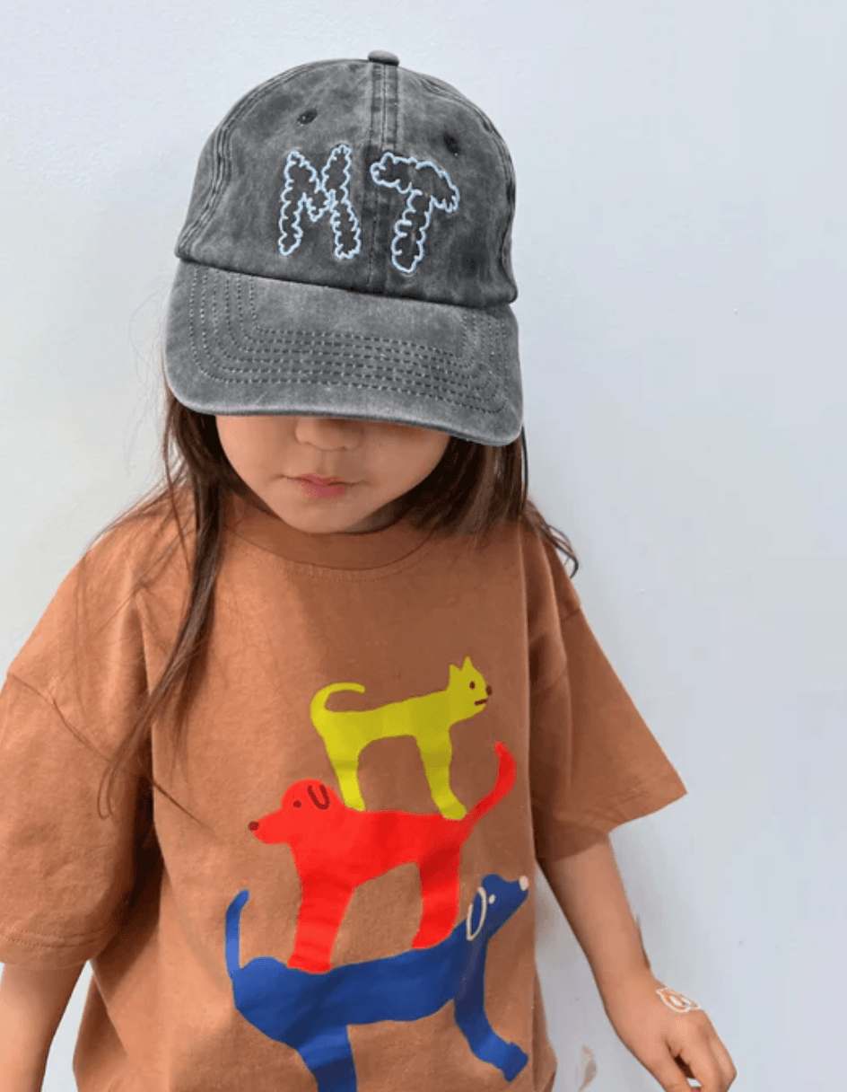 Child wearing a brown shirt with colorful dog graphics and a gray cap with 'MT' on a white background