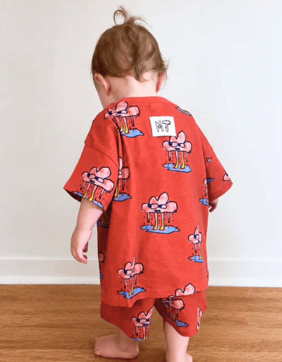 Child wearing a red outfit with cartoon designs on a wooden floor.