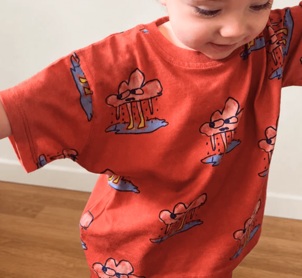 Child wearing a red shirt with cartoon character prints on a wooden floor.