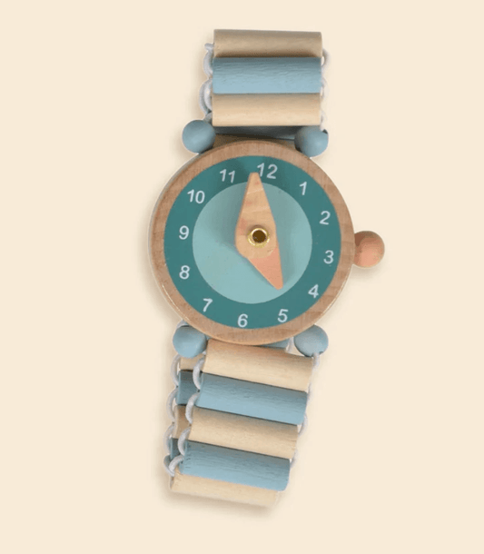 A wooden toy watch with a round face, light blue and beige striped links, and a peach-colored hour hand, shown on a solid cream background.