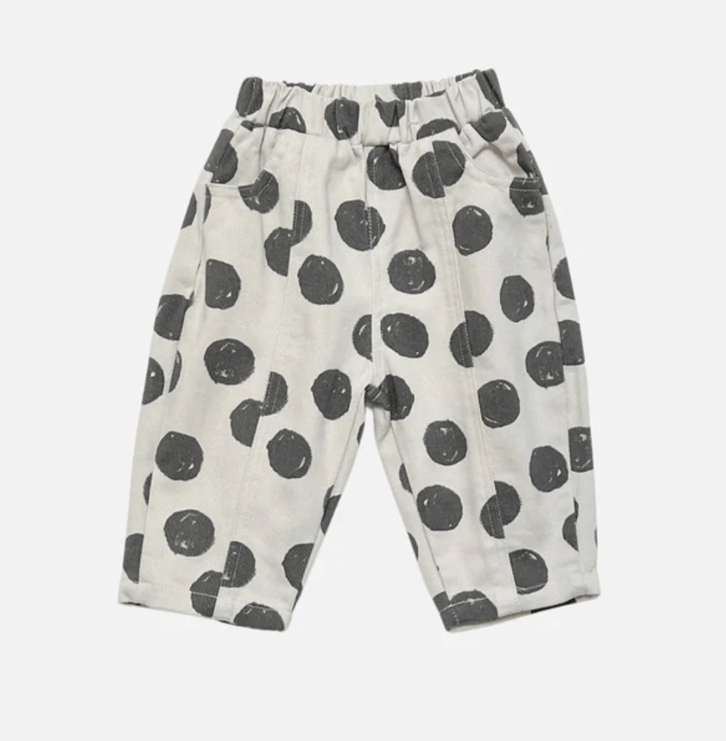 A pair of toddler's cropped pants in a warm off-white fabric with a dark gray hand-drawn polka dot pattern, featuring an elastic waistband and side pockets.