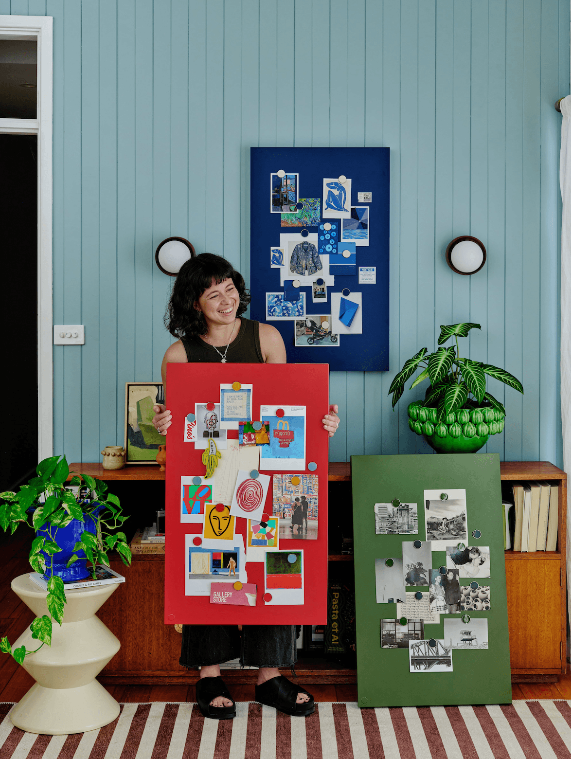 Woman holding a red collage in a room with blue walls and various artworks.