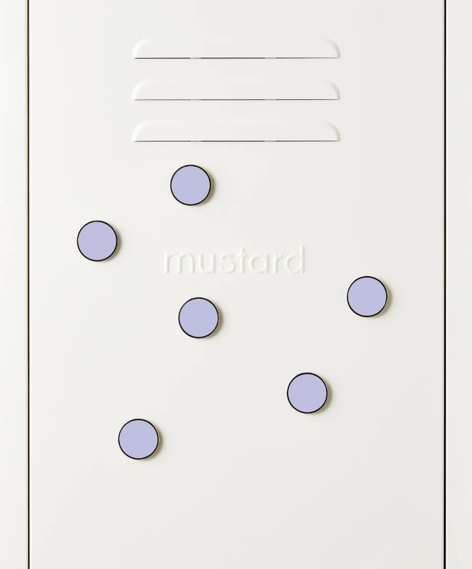 A close-up of a white surface with the word 'mustard' printed in lowercase and five light lavender oval magnets arranged on top. Three horizontal slots are visible near the top.