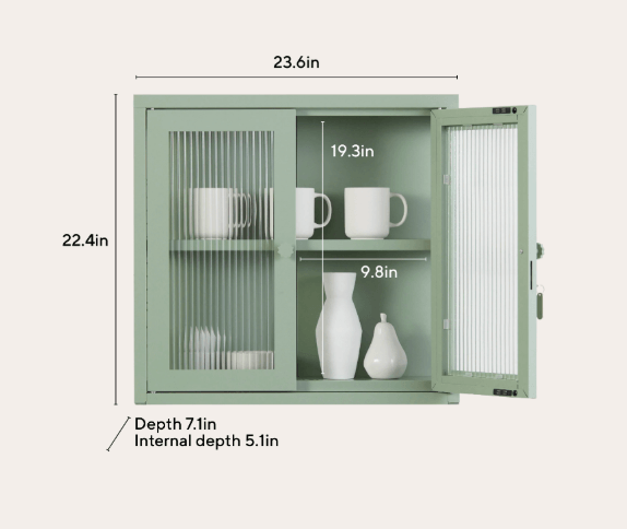 A sage green wall-mounted cabinet with two glass-paneled doors, shown open with white ceramic mugs and vases inside. Measurement labels and arrows indicate dimensions including 23.