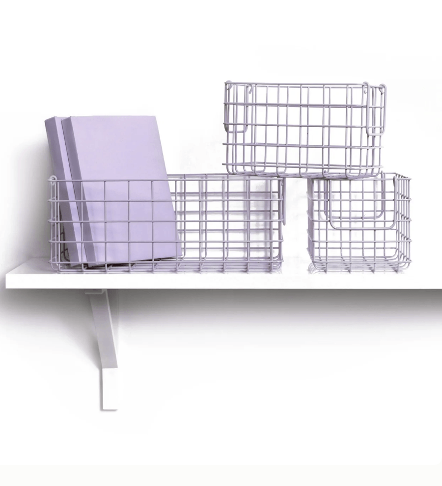 Three purple  wire mesh storage baskets arranged on a white shelf, with a lavender notebook placed inside one basket, against a clean white background.