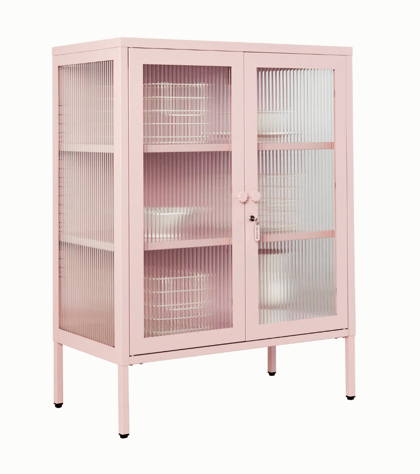 A light pink metal cabinet with two ribbed glass doors and three interior shelves, shown on a plain white background.