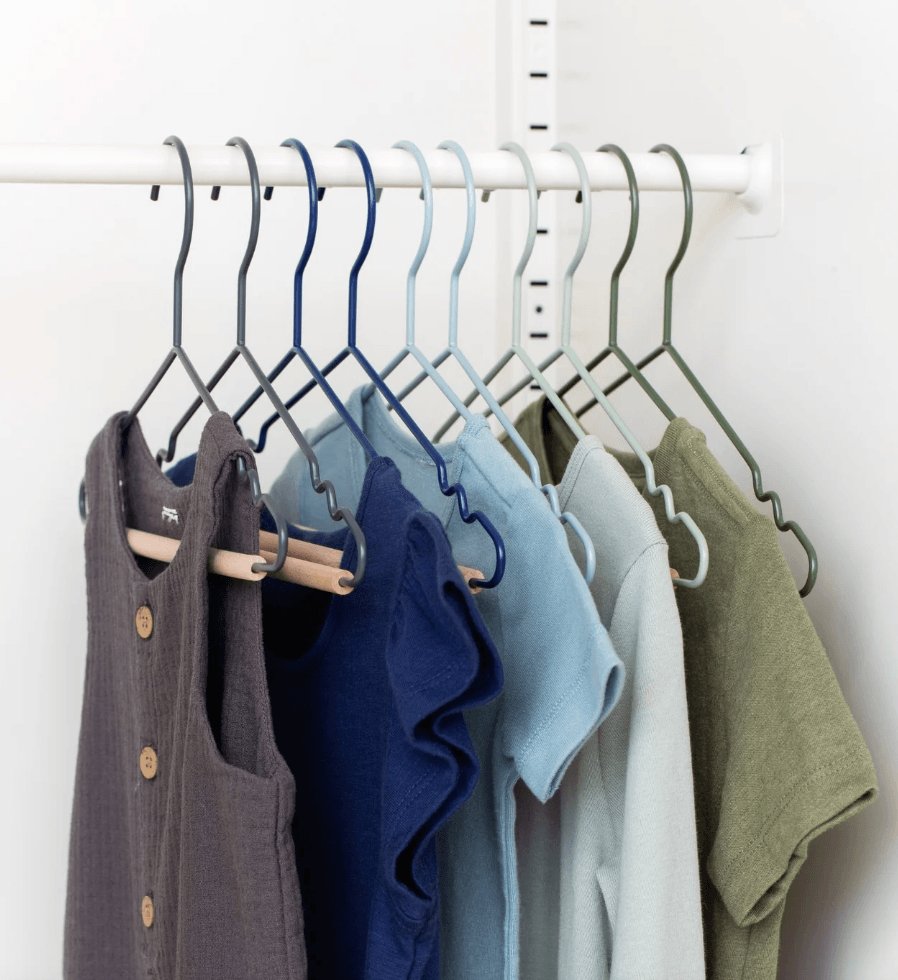 A set of wavy metal hangers in multiple colors (gray, blue, light blue, sage green) hanging on a white rod, holding several shirts and tops.