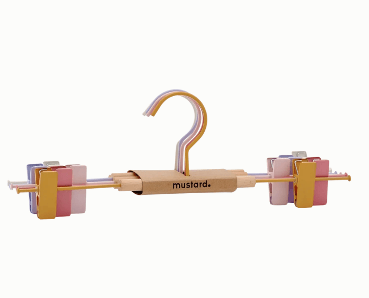 Metal pants hangers with a colorful pastel striped hook and side clips, featuring a cardboard center label that reads 'mustard+'.
