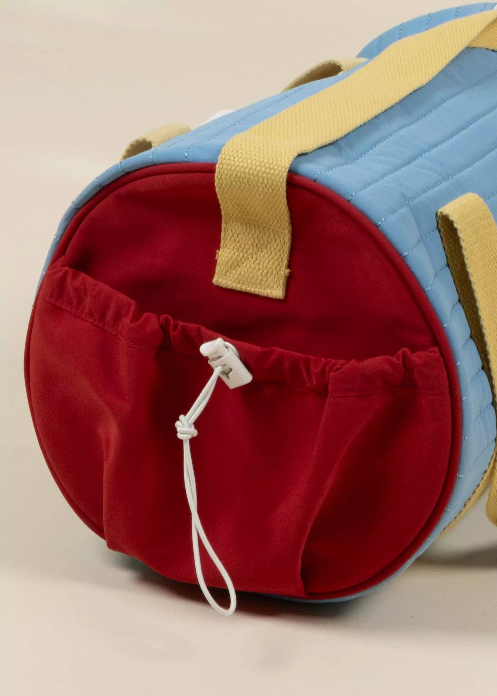 Red and blue duffel bag with yellow strap on a beige background