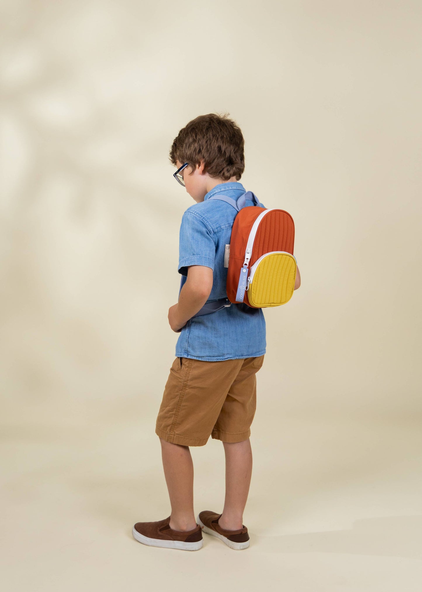 Child wearing a colorful backpack on a beige background