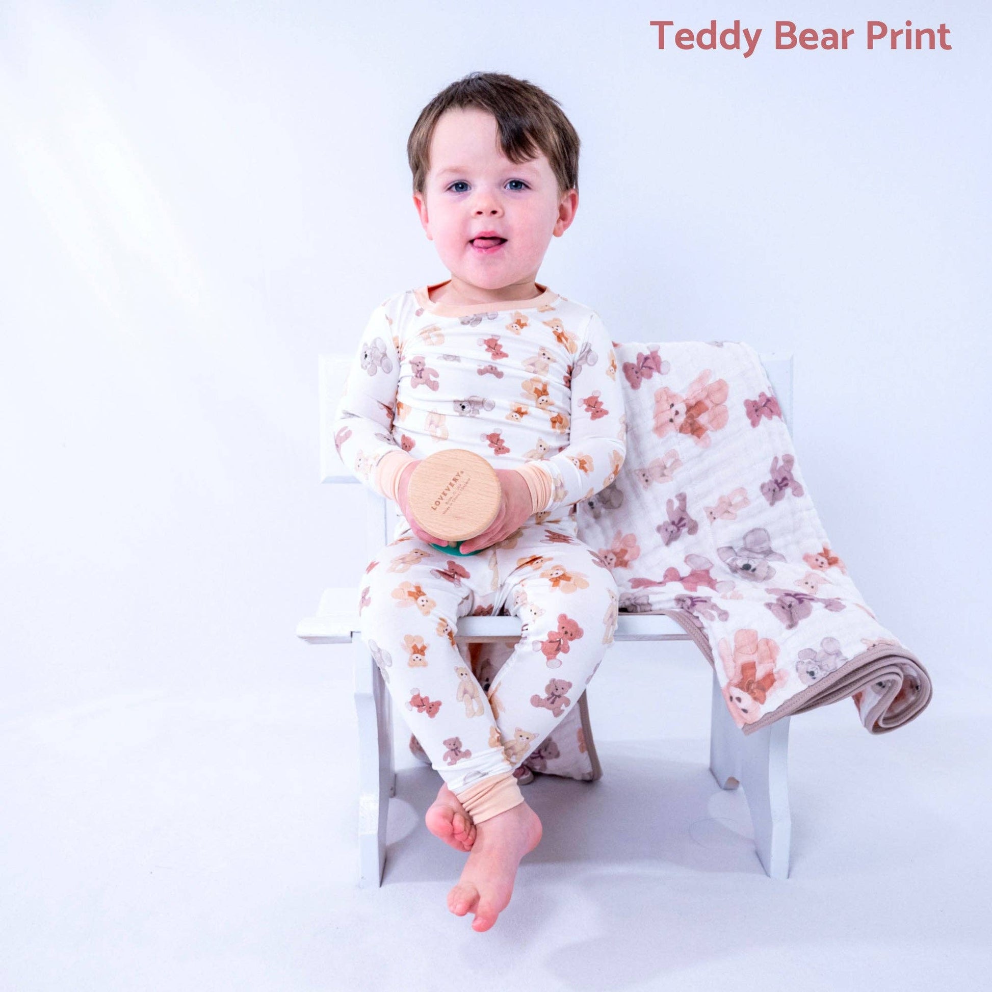 Child wearing teddy bear print pajamas sitting on a chair with a matching blanket.