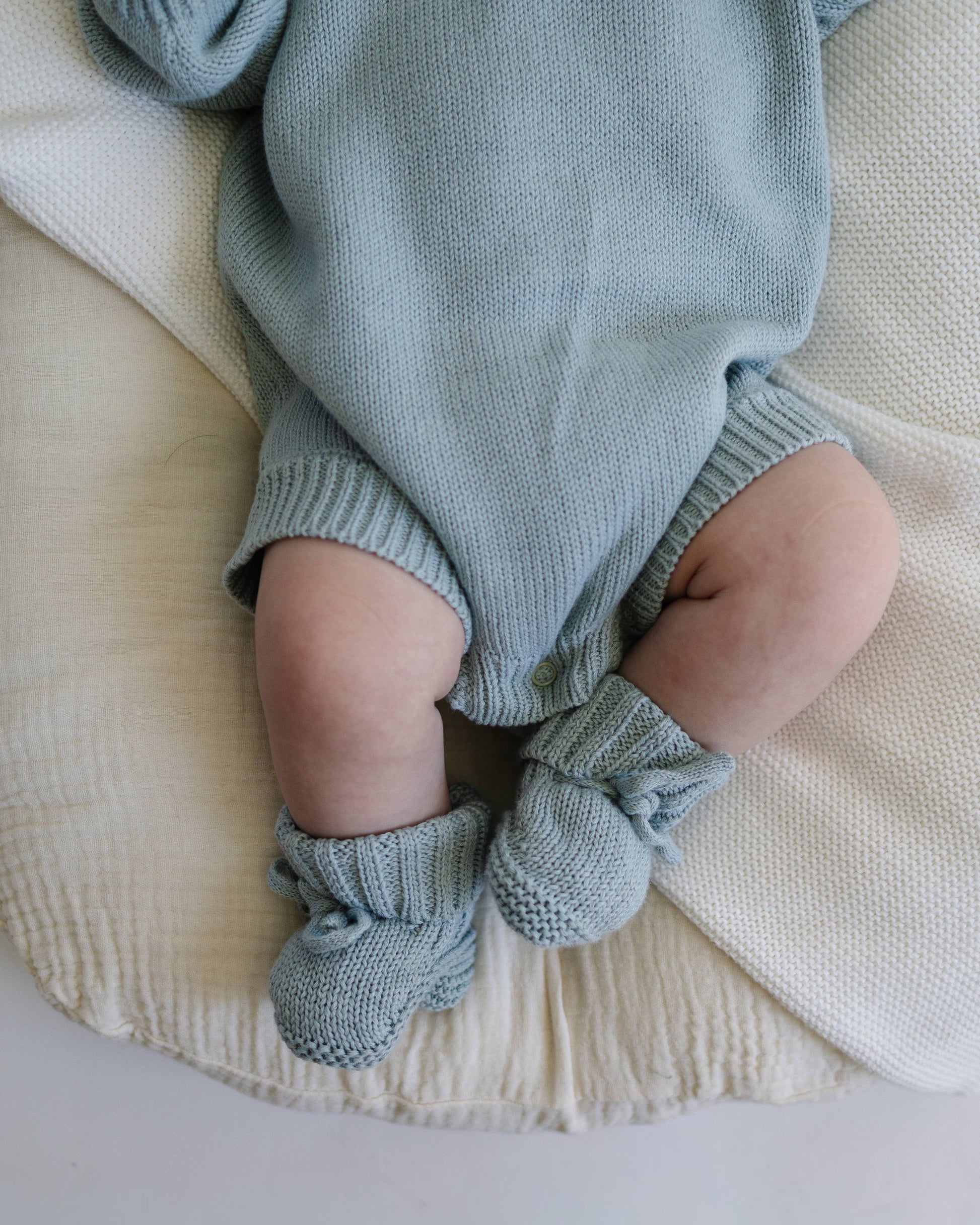 Baby in a light blue knitted outfit lying on a beige blanket
