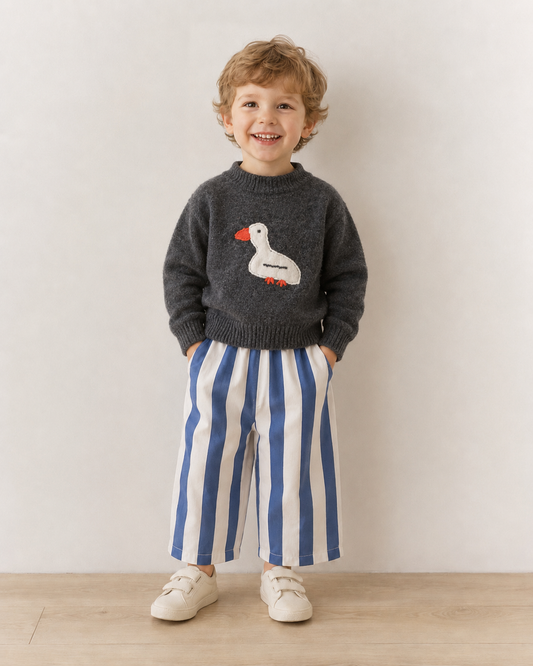 Child wearing a dark sweater with a duck design and blue and white striped pants against a plain background