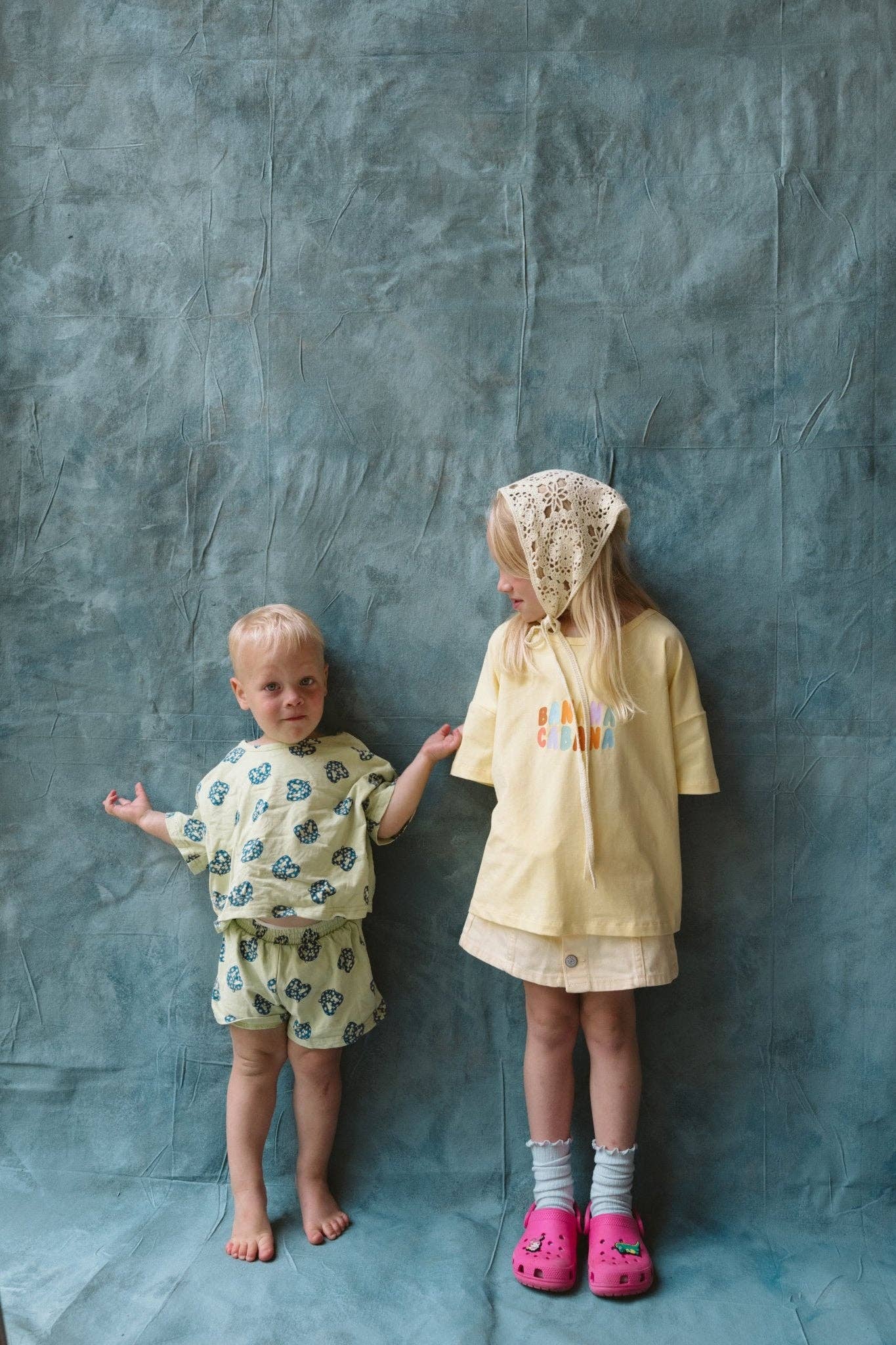 Two children in patterned outfits standing against a textured gray background