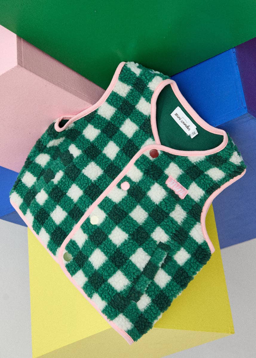 A green and white checkered fleece vest with pink trim, laid flat on colorful geometric blocks.