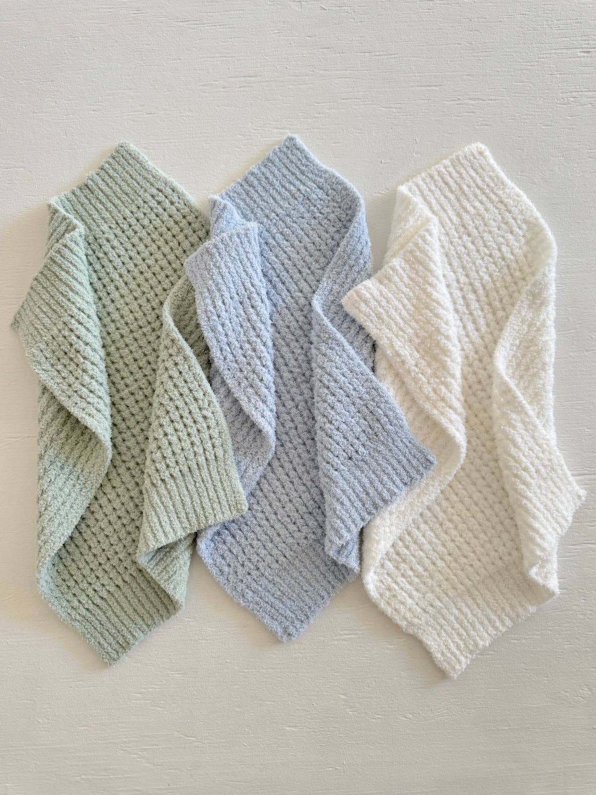 Three textured baby blankets in green, blue, and white on a light gray background