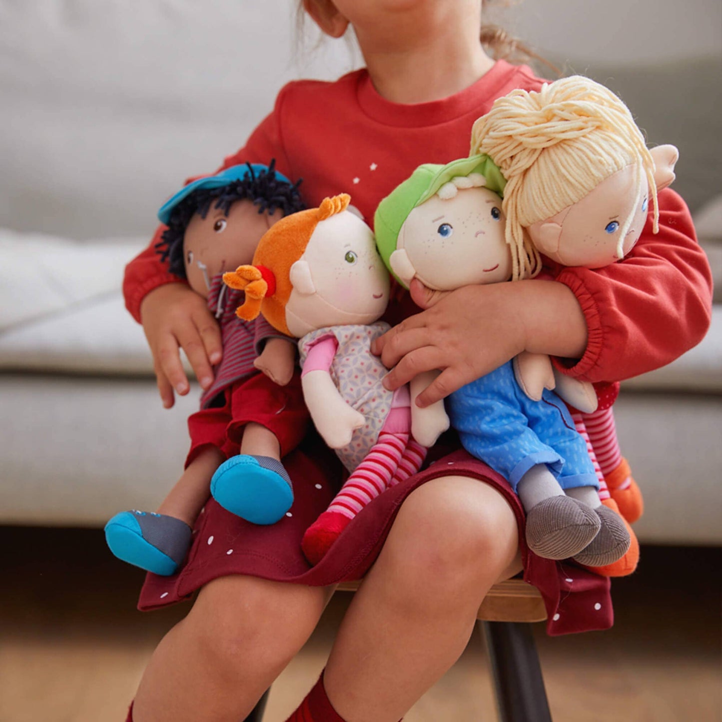 Child holding a group of colorful dolls on a chair