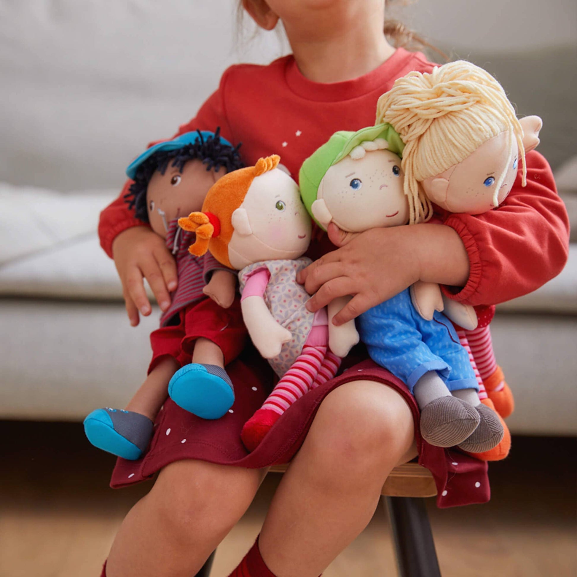 Child holding a group of colorful dolls on a chair