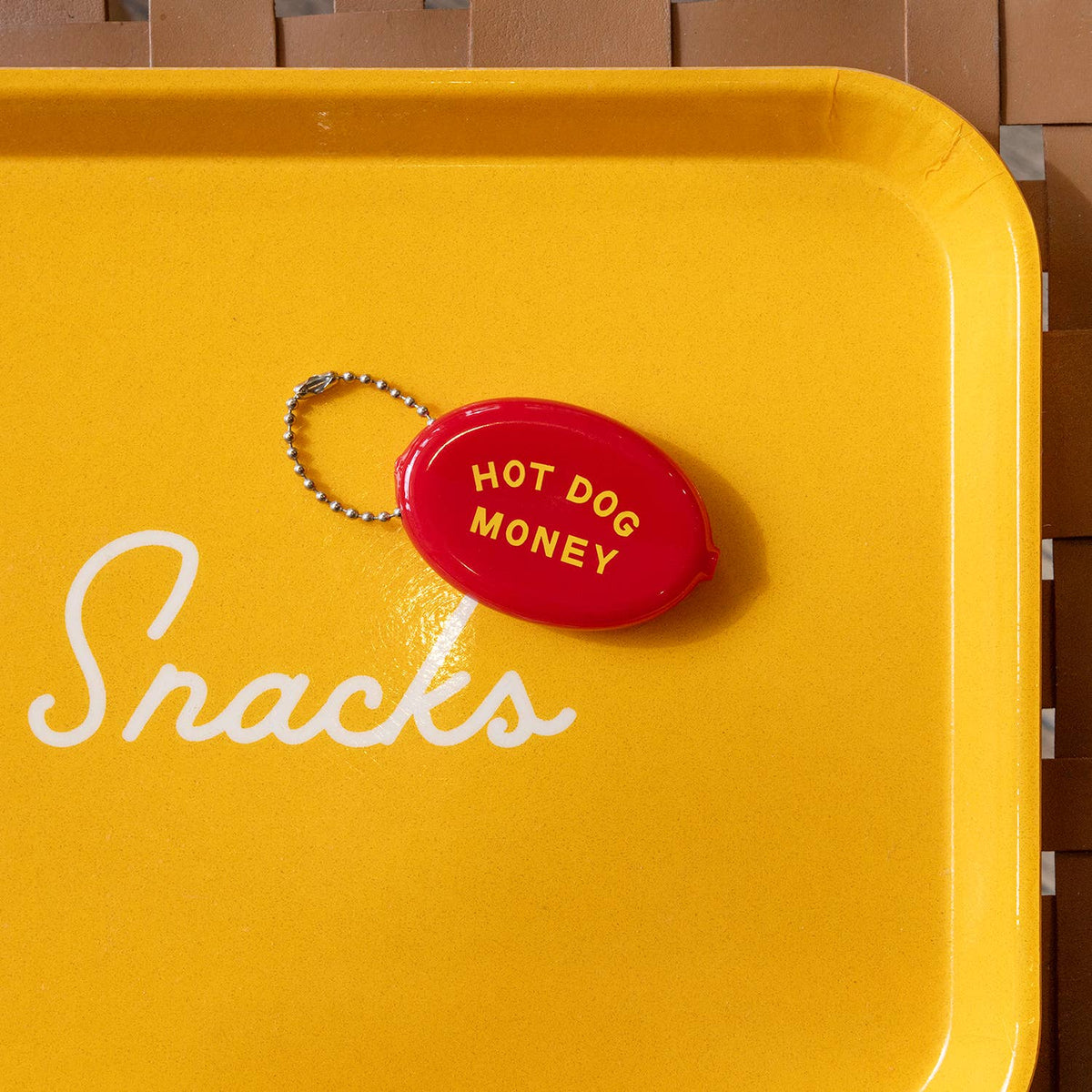 Yellow tray with 'Snacks' text and a red 'Hot Dog Money' keychain on a wooden surface.