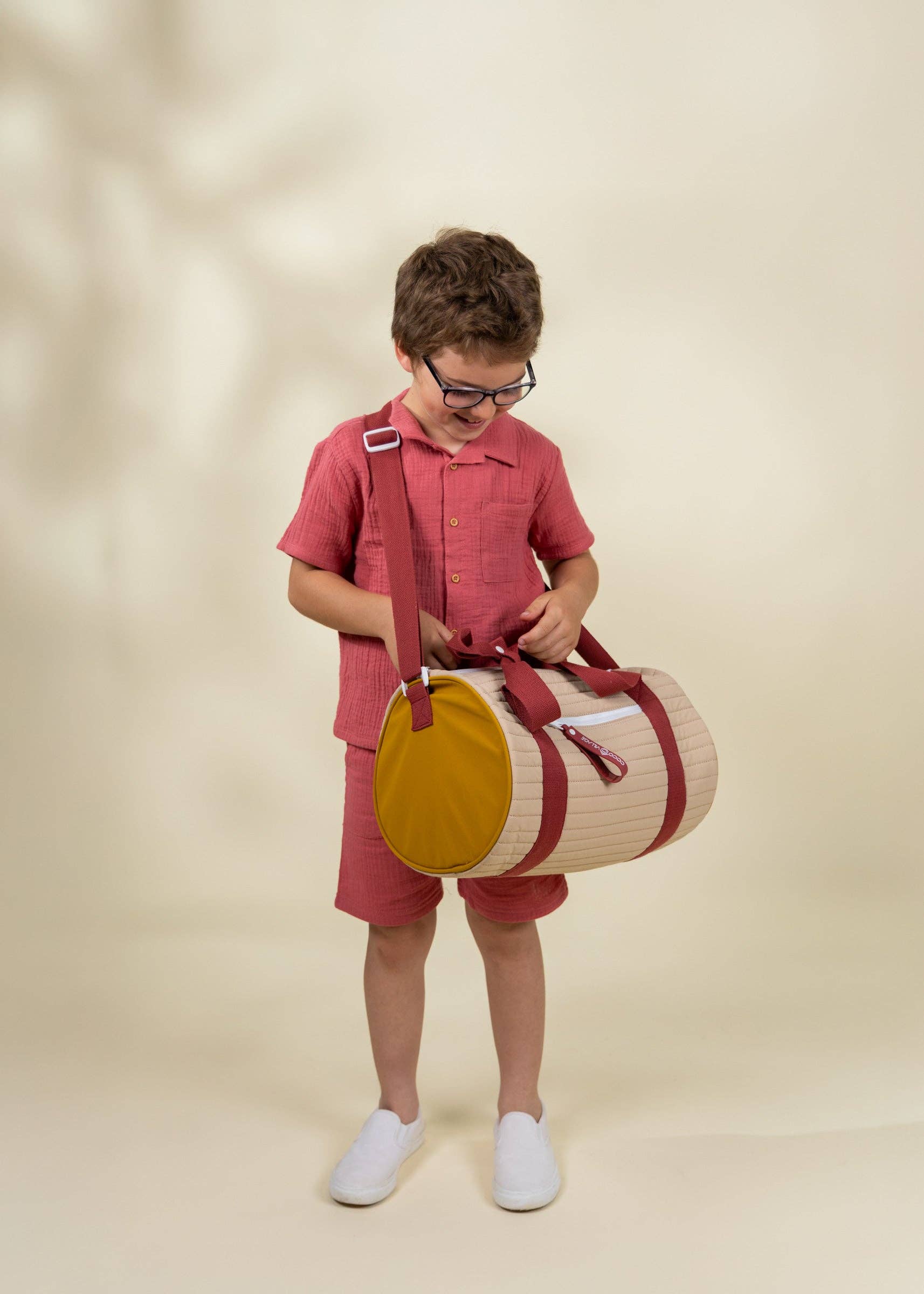 Child holding a round bag with a strap against a beige background