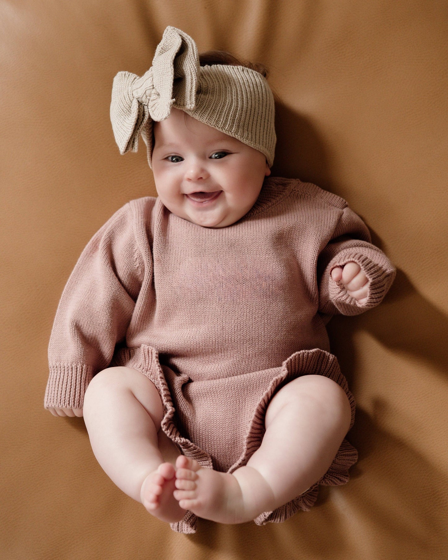 Baby in pink outfit with headband against a brown background