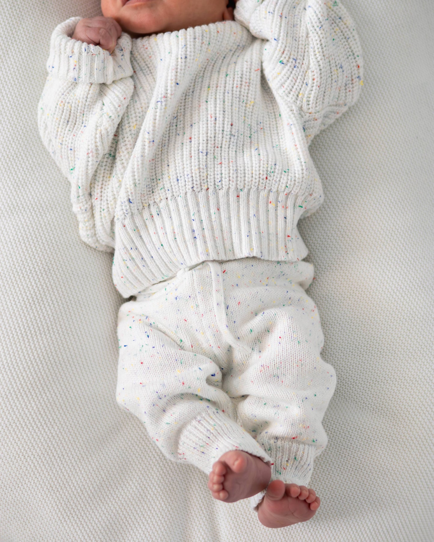 Baby wearing a white knitted outfit on a light gray background