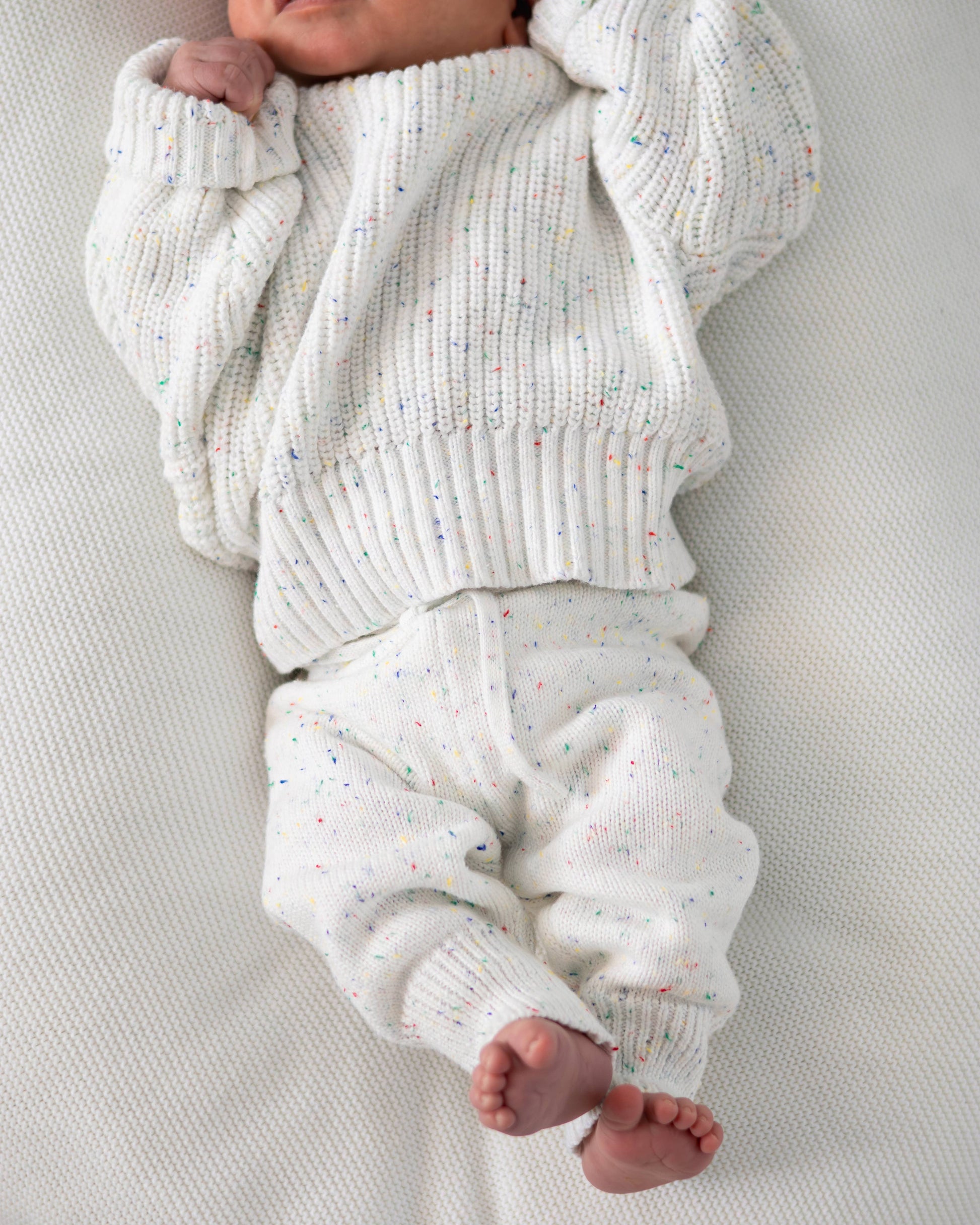 Baby wearing a white knitted outfit on a light gray background