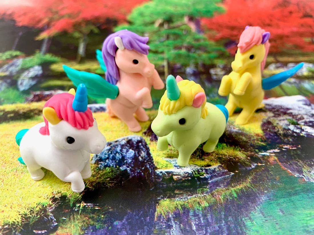 Colorful unicorn figurines on a fantasy landscape with trees and rocks.