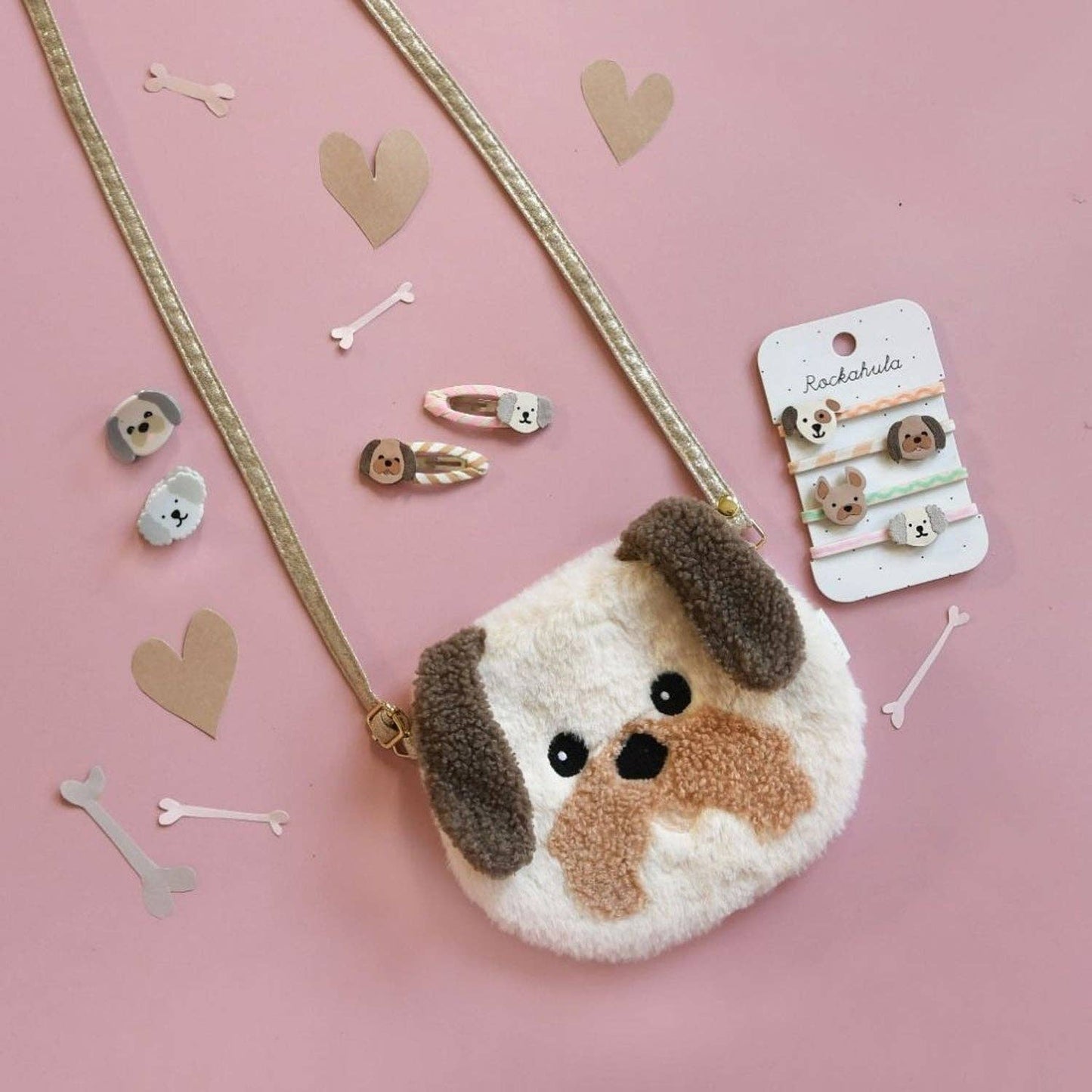 Fluffy dog-shaped purse with decorative hair clips on a pink background