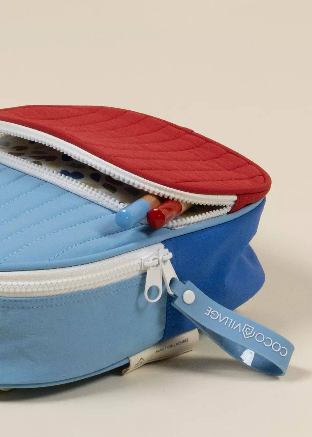 Blue and red pencil case with a visible brand label on a beige background