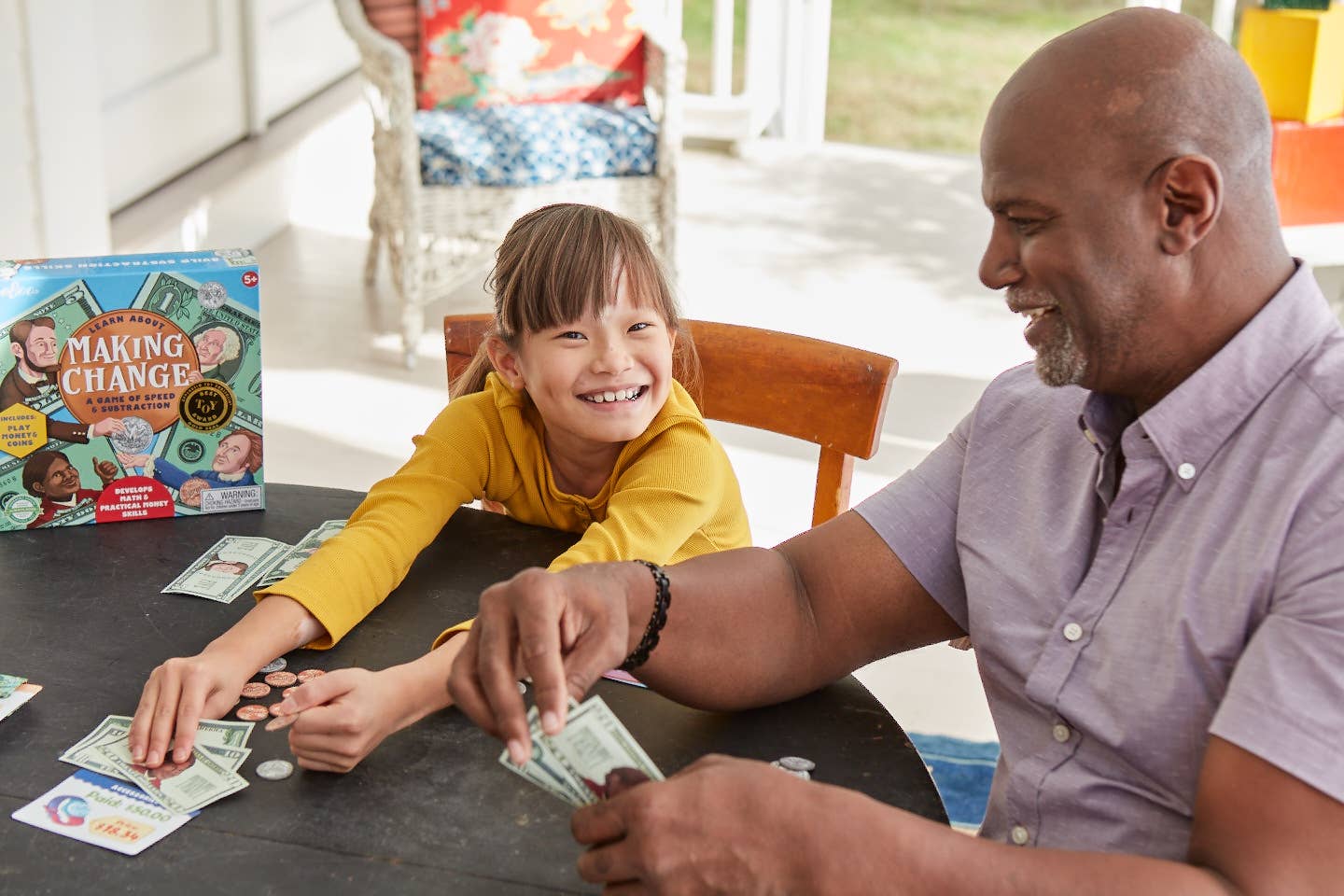 Man and child playing with money at a table, with a 'Making Change' game box in the background.